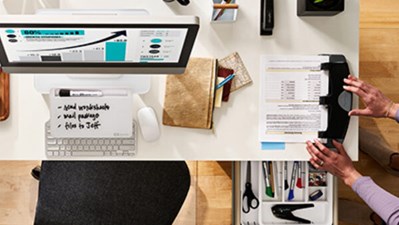 Assorted Swingline products on a desk with a woman using a 3-hole punch.